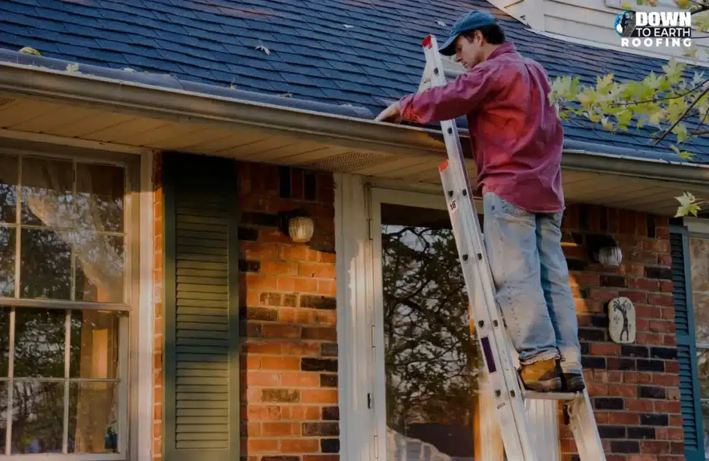 Worker on a ladder cleaning debris from a home’s gutter to maintain proper roof drainage